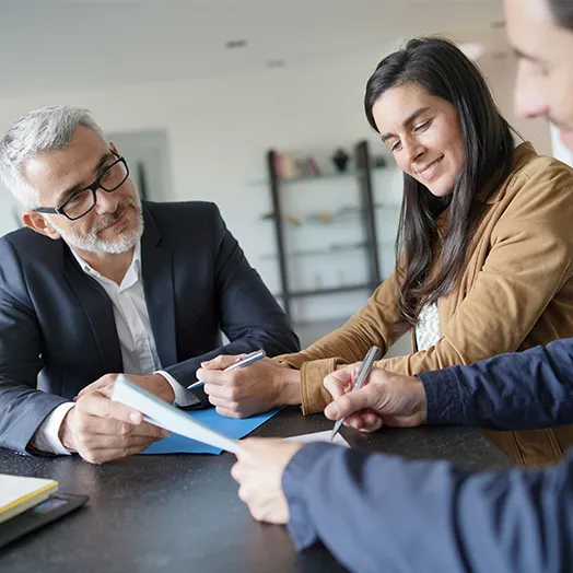 distiguished looking man holding a document for a young couple sitting at a table getting ready to sign