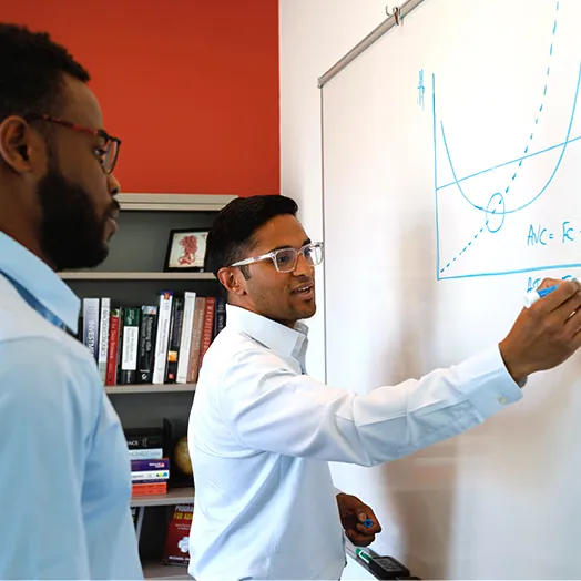 two people standing at a whiteboard with equations on it
