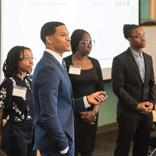 four students standing at the front of the classroom