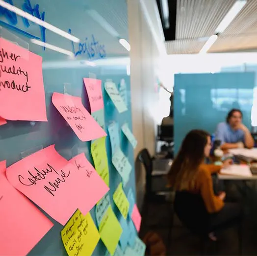 two students in background with deep perspective and sticky notes on a wall upclose