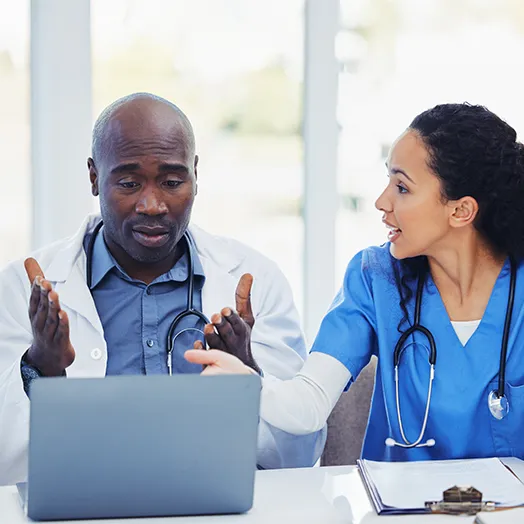 two seated doctors discussing an AI diagnosis or treatment behind a laptop on a table