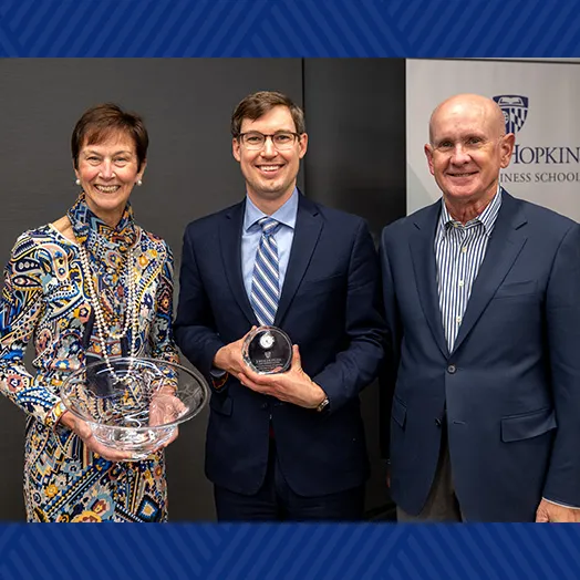Christopher Myers (center), inaugural Peetz Family Professor of Leadership, accepting an award from Karen Peetz (left), with a male attendee/speaker at the installation event (right).